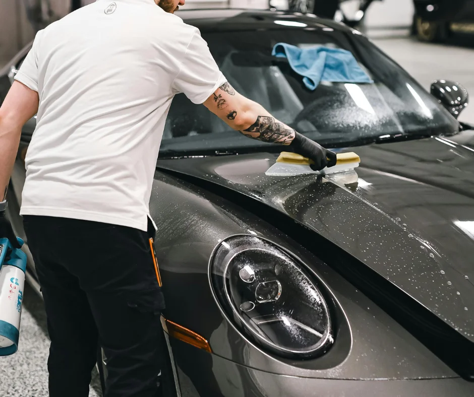 Detailer working on the wet hood of a gray Porsche 911 at the shop